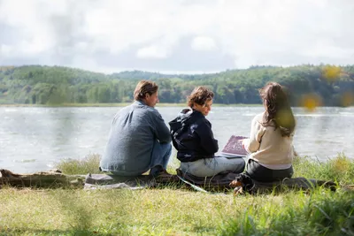 Three people sitting on a blanket by the water in Lietzow on Rügen, one showing something on a tablet