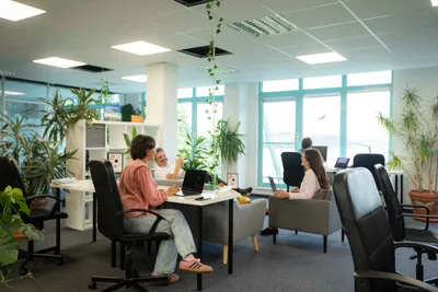 Open coworking room with desks, armchairs and lots of plants, several people working and talking